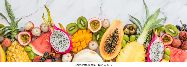 Fresh Exotic Fruits And Tropical Palm Leaves On White Marble Background - Papaya, Mango, Pineapple, Passion Fruit, Dragon Fruit, Melon. Mockup, Flat Lay, Overhead. Top View.