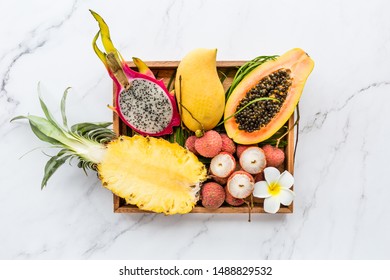 Fresh Exotic Fruits In Wooden Box On White Marble Background - Sliced Papaya, Mango, Pineapple, Dragon Fruit, Lychee. Mockup, Flat Lay, Overhead. Top View.