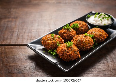 Fresh falafel with parsley and tzatziki sauce in black plate on wooden table.