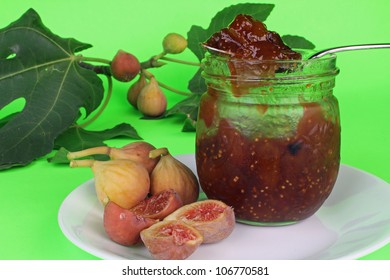 Fresh Figs And Jar Of Preserves On Plate With Fig Tree Branch And Leaves On Bright Green Background.