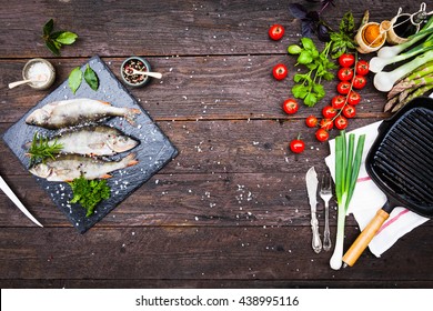 Fresh fish with aromatic herbs, spices, salt, bottles with olive oil and balsamic vinegar,perch on slate tray on a wet dock, on dark vintage background, top view, healthy food, diet or cooking concept - Powered by Shutterstock