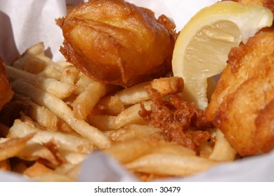 Fresh Fish And Chips In A Wicker Basket With Butcher Paper And A Lemon Wedge Are About To Be Eaten By The Photographer