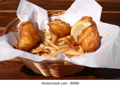 Fresh Fish And Chips In A Wicker Basket With Butcher Paper And A Lemon Wedge Are About To Be Eaten By The Photographer