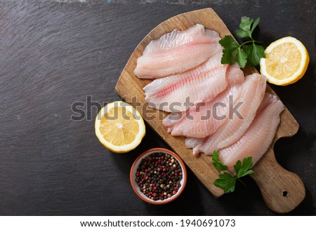 fresh fish fillet of tilapia with ingredients for cooking on wooden board, top view