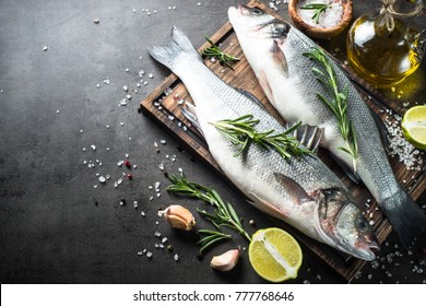 Fresh fish seabass and ingredients for cooking. Raw fish seabass with spices and herbs on black slate table. Top view with copy space.