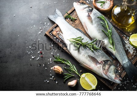 Fresh fish seabass and ingredients for cooking. Raw fish seabass with spices and herbs on black slate table. Top view with copy space.