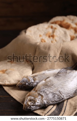 Fresh flatbreads and dried fish on wooden table against dark background, closeup