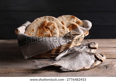 Fresh flatbreads and dried fish on wooden table against black background, closeup