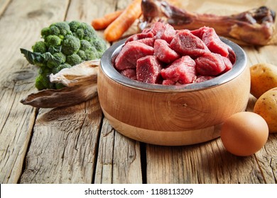 Fresh food for a healthy pet with chopped beef, eggs, broccoli, vegetables and a large meaty bone on a rustic wood floor