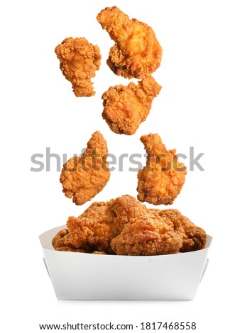 Fresh fried chicken falling into container on white background