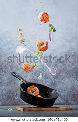 Fresh fried shrimp fly into a pan. Sea food with garlic, onion, cream, spices and basil flying into a pan on modern concrete background. Food preparation, meal ready for cooking.