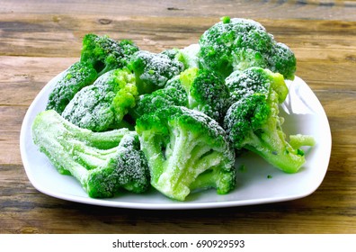 Fresh frozen broccoli on white plate, wooden table, healthy diet food, closeup