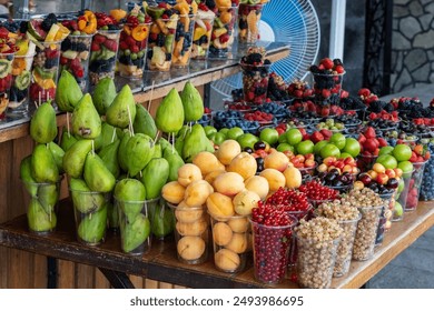 Fresh fruit and berries in plastic cups on a wooden counter waiting for sale. Includes figs, currants, apricots, cherries, blackberries, and more. - Powered by Shutterstock