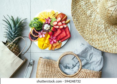Fresh fruit plate and set of summer fashion beach accessories, top view from above (overhead). Tropical beach lifestyle.