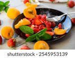 fresh fruit salad of ripe strawberries and apricots, on a light wooden table .