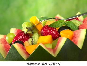 Fresh fruit salad (strawberry, kiwi, mango, grape) in melon bowl with kiwi and mango on fork and mint leaf as garnish (Selective Focus, Focus on the fruit on the fork and the mint leaf) - Powered by Shutterstock