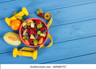 Fresh fruit salad, tape measure and dumbbells for using in fitness, concept of sport, diet, slimming, healthy lifestyles and nutrition
