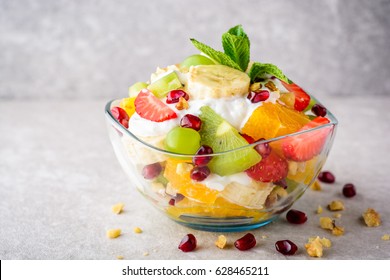 Frischer Obstsalat mit Jogurt und Walnüssen in einer Glasschüssel auf Steinhintergrund. Gesund essen. Selektiver Fokus.