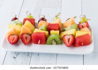 brochetas de fruta fresca sobre una bandeja sobre una mesa blanca de madera.