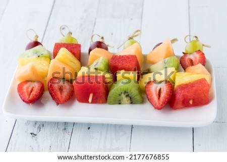 Fresh fruit skewers on a small platter on a white wash wooden table.