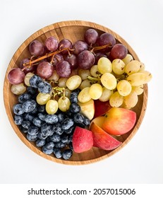 Fresh fruits and berries on the wooden plate in white background: grapes, blueberries, apple. Top view.