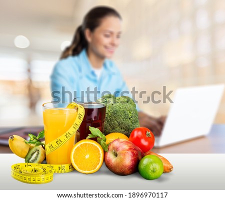 Fresh fruits with measuring tape and glass on office desk against blurred woman with laptop.
