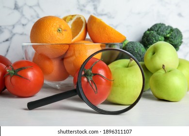 Fresh fruits, vegetables and magnifying glass on white table. Poison detection