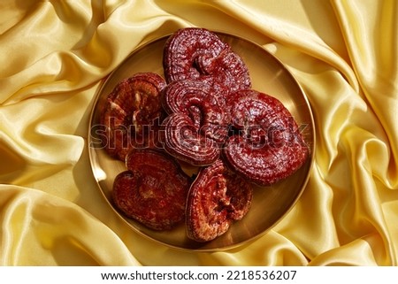 Fresh Ganoderma mushrooms are displayed on a gold tray against a yellow silk backdrop.