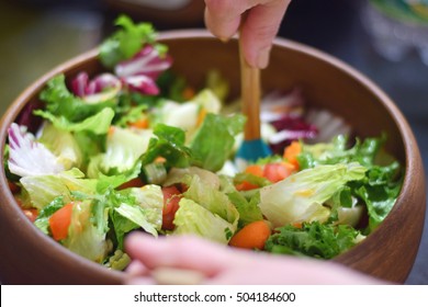 Fresh garden salad being tossed in a stylish wooden bowl