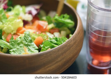 Fresh garden salad in a stylish wooden bowl next to a glass of cranberry juice