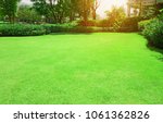 Fresh gardening green Bermuda grass smooth lawn with curve form of bush, trees on the background in the house