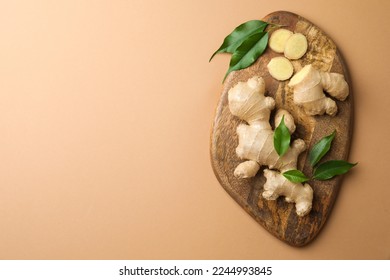 Fresh ginger with green leaves on light pale brown background, top view. Space for text - Shutterstock ID 2244993845