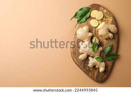 Fresh ginger with green leaves on light pale brown background, top view. Space for text