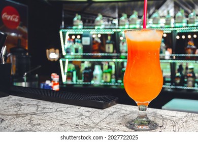 Fresh Glass Of Tropical Cocktail With Juice On The Background Of The Bar Counter. Cocktail Glass With Ice And Festive Lights In The Background.