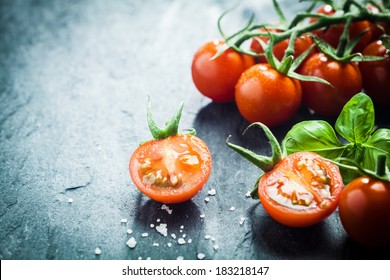 Fresh grape tomatoes with basil and coarse salt for use as cooking ingredients with a halved tomato in the foreground with copyspace - Powered by Shutterstock