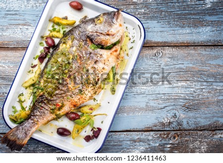 Fresh Greek barbecue gilthead seabream with peperoni and Kalamata olives as top view in a white skillet 