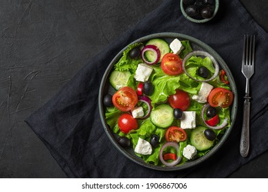 Fresh greek salad with olives, feta cheese, tomato, cucumber, onion with fork on towel on black background. top view. vegetarian food