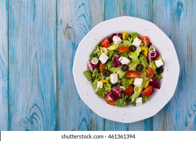 Fresh Greek Salad On A Plate. Blue Wooden Board. Top View.