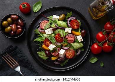 Frischer griechischer Salat mit Tomate, Gurken, Bierpfeffer, Oliven und Feta-Käse auf schwarzem Teller, Draufsicht, dunkler Hintergrund