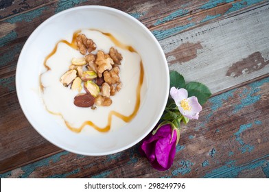 Fresh Greek Yogurt Topped With Nuts And Seeds, A Drizzle Of Honey And Served On A Rustic Wooden Table With Fresh Wild Flowers.