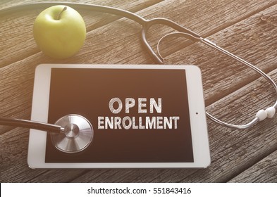 Fresh green apple and stethoscope with word OPEN ENROLLMENT on digital tablet against wooden table. Medical Concept.