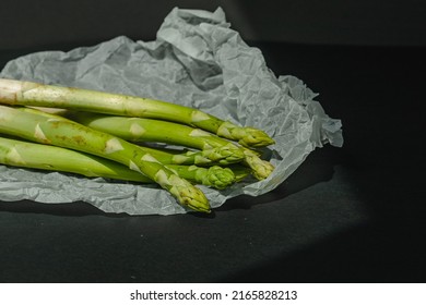 fresh green asparagus lies on a white parchment on a dark gray background. proper nutrition. Lifestyle. place for text