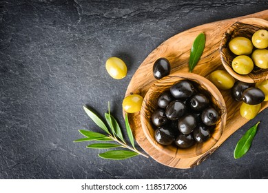 Fresh Green And Black Olives On Dark Stone Table Or Board. Olive Leaves, Wooden Pickers On Black Blackground.