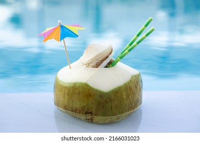 Fresh  Green Coconut Drink With Paper Straw  And Rainbow Umbrella  Swimming  In Pool  Water Background  . Centre Composition Vacation Card , Vacation  Exotic  Resort  Travel Destinations  Concept .