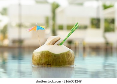 Fresh  Green Coconut Drink With Paper Straw  And Rainbow Umbrella  Swimming In  Pool  Water  On  Resort Spa Hotel Background With Copy Space . Vacation  Exotic  Travel Destinations  Concept .