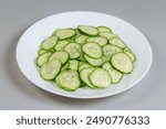 Fresh green cucumbers cut into thin circles on a dish on a gray background
