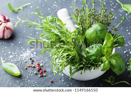 Fresh green garden herbs in mortar bowl and spices on black stone table. Thyme, rosemary, basil, and tarragon for cooking.