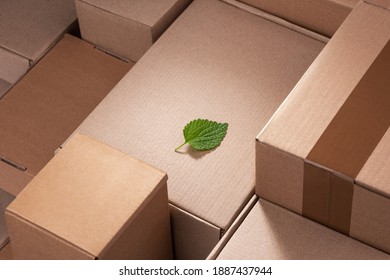 Fresh green leaf laying between cardboard boxes. Shipping deliveries, global trade and environmental impact. - Shutterstock ID 1887437944