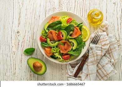 Fresh green lettuce salad with smoked salmon and avocado on wooden background