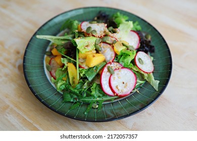Fresh green mixed salad with radish, mango and lettuce on a plate. Top view, close-up.